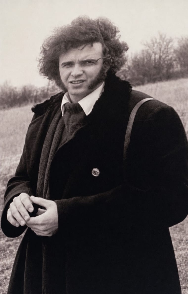 Franz Groihs als junger Mann. Schwarz-Weiß-Aufnahme in einem winterlichen Feld, dunkler Mantel, der Blick geht zur Kamera.